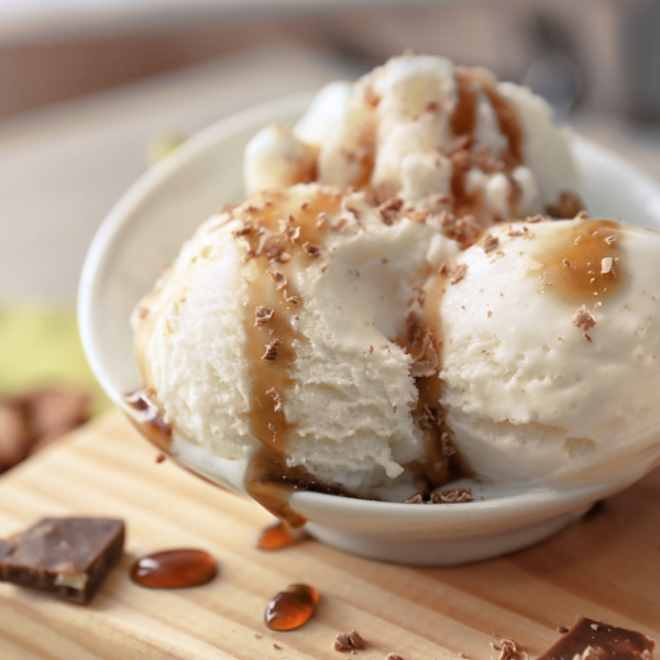 Ice cream with caramel a white bowl on a wooden surface.