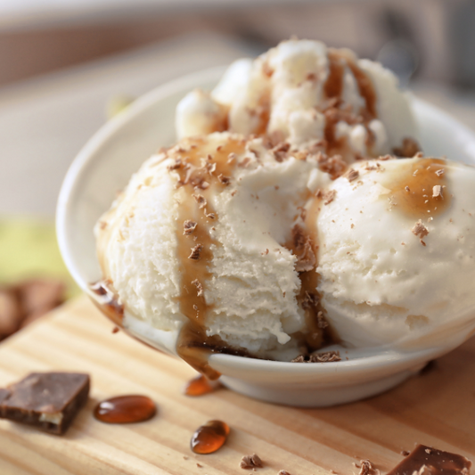 Ice cream with caramel a white bowl on a wooden surface.